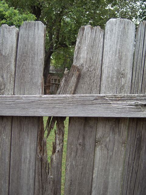 A weathered wood privacy fence with broken, leaning boards